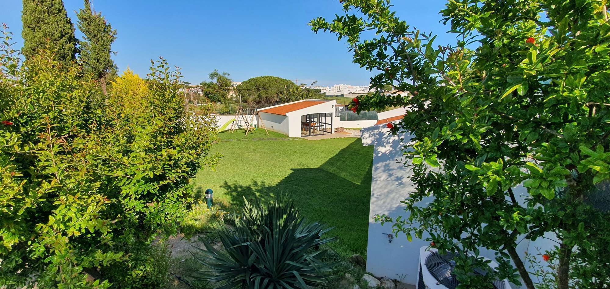 A residential property with a well-maintained lawn, a white building with a red roof, and surrounding greenery.