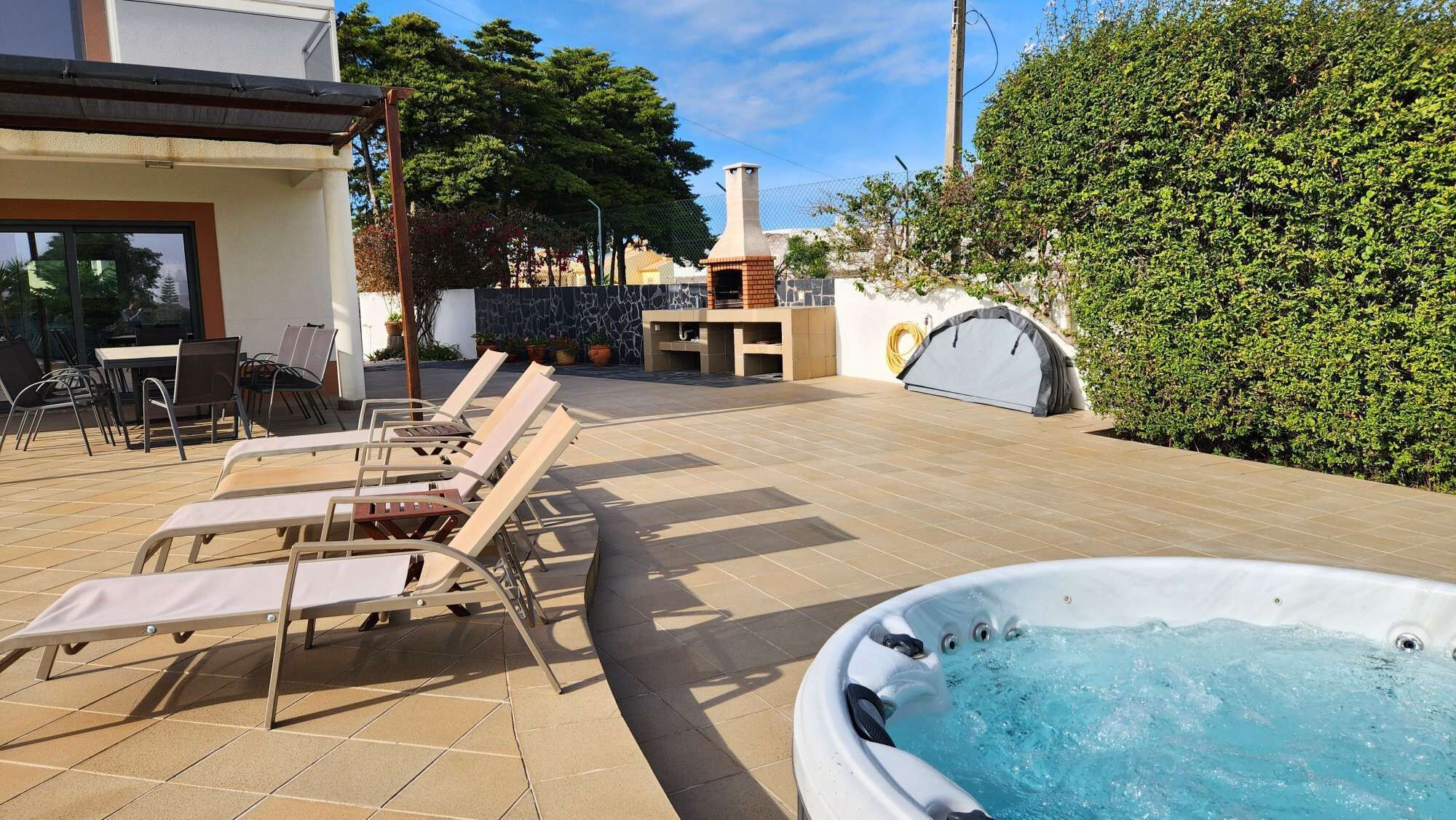 A patio with lounge chairs, a hot tub, and a brick oven.