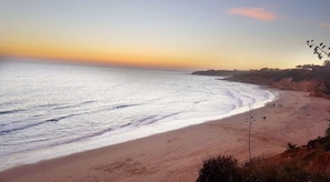 A beach with a clear sky, waves, and a few people.