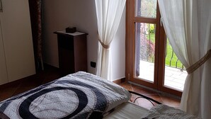 Une chambre avec deux lits, un plancher en bois, une fenêtre avec des rideaux légers et une vue sur la verdure.