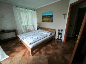A bedroom with a bed, a nightstand, a lamp, a painting on the wall, and a door leading to another room.