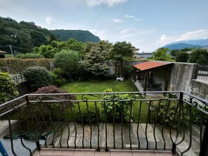 A balcony with a view of a well-maintained garden and a building with a red roof.