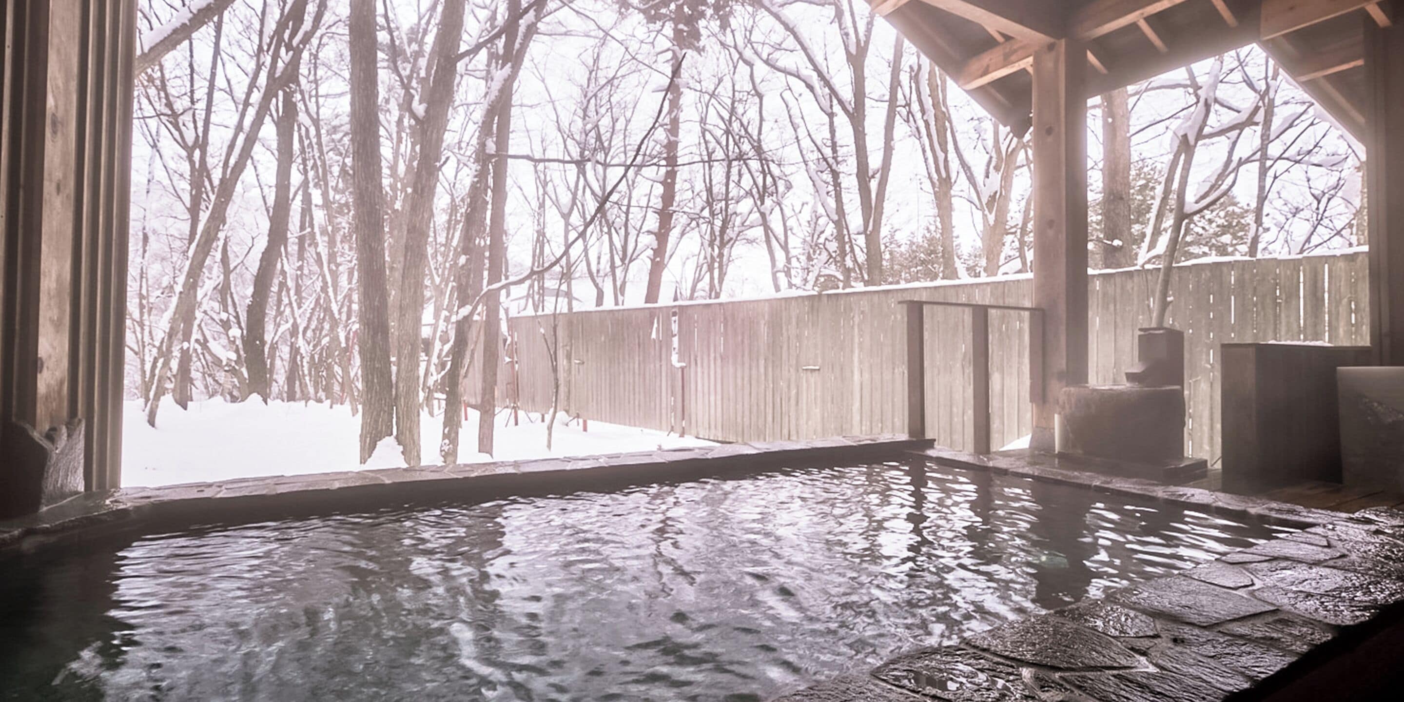 Ein Whirlpool mit einer Holzterrasse und Blick auf schneebedeckte Bäume.