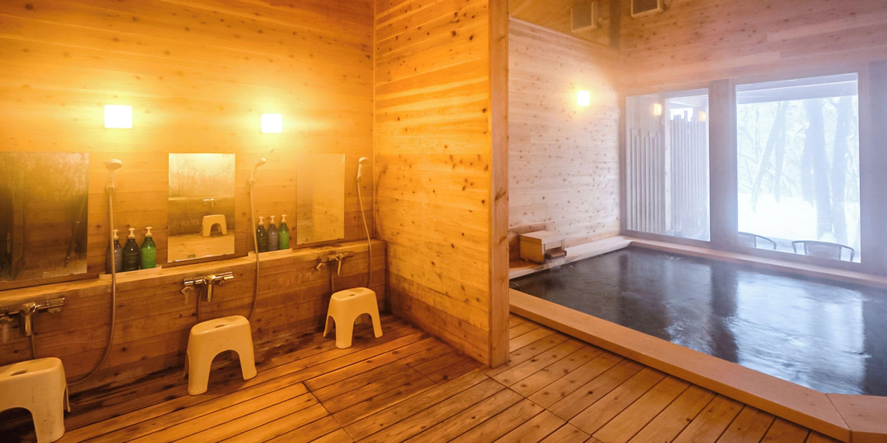 L’intérieur d’un chalet en bois, avec un plancher en bois, un grand miroir, une baignoire et une fenêtre donnant sur les arbres.