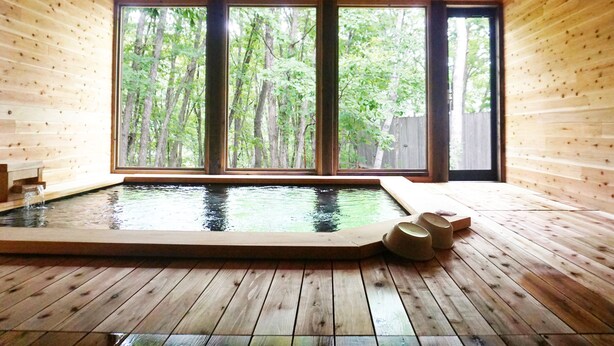 A wooden cabin with a hot tub and large windows overlooking a forest. - Hotel Abest Happo Aldea (Hakuba)