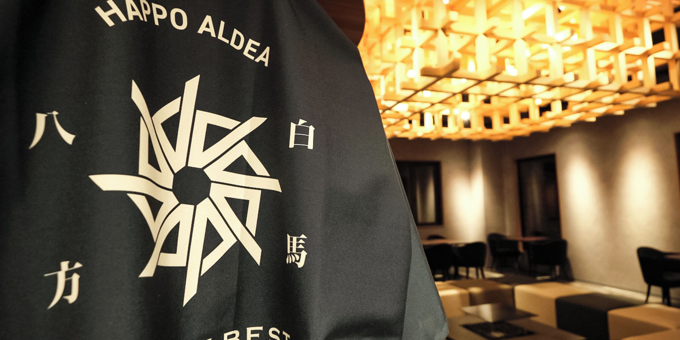 A black t-shirt with white text and a geometric design, hanging in a modern interior with a geometric light fixture.