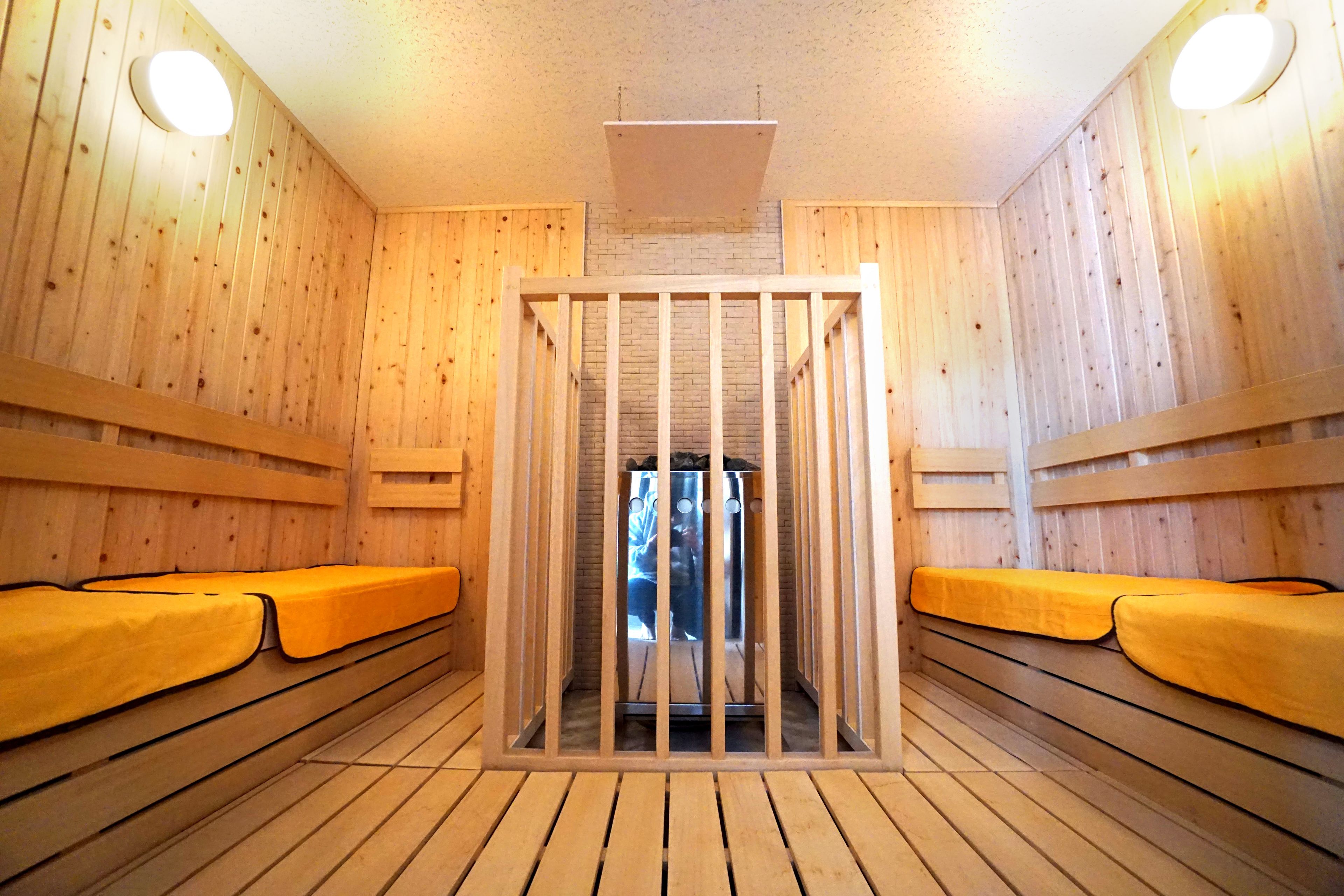 Un sauna avec des murs et des bancs en bois, une porte centrale et des luminaires au plafond.