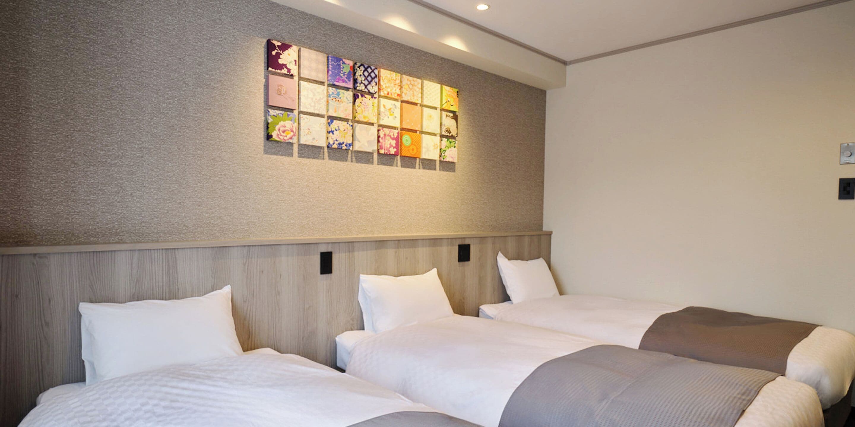 Une chambre d’hôtel avec trois lits, une tête de lit en bois et une œuvre d’art murale au-dessus des lits.
