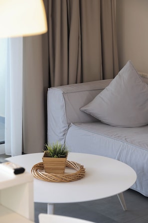 En moderne stue med en grå sofa, et rundt hvidt bord og en lille træpotte med grønne planter.