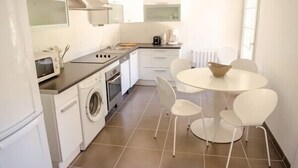 A compact kitchen with a washing machine, a stove, and a dining area with a round table and four chairs. -  Large apartment with terrace in character property (Béziers)