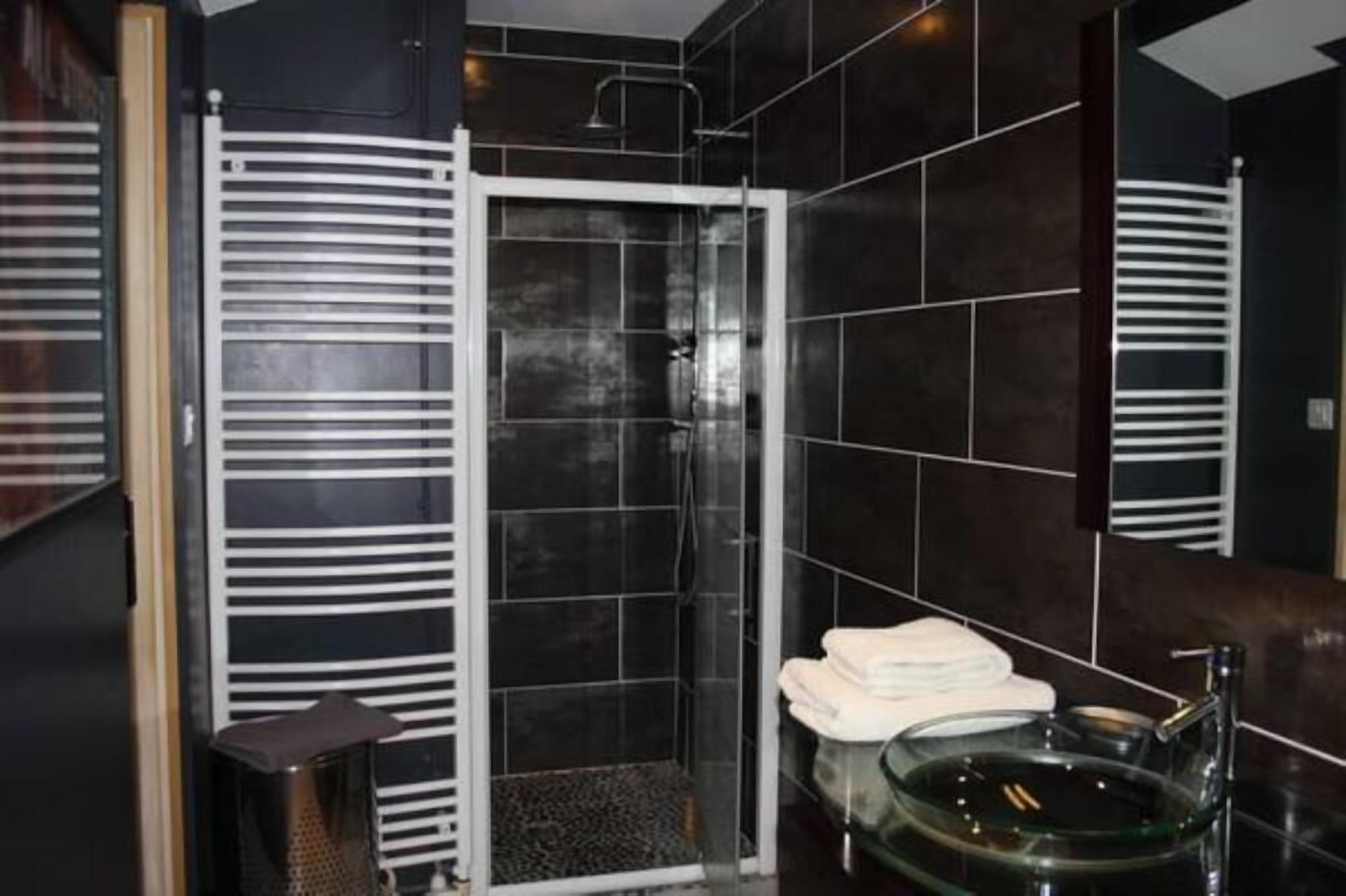 Une salle de bain moderne avec des carreaux de couleur foncée, une douche en verre, un lavabo en verre et un porte-serviettes.