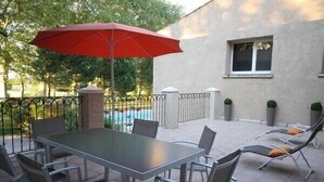 An outdoor patio with a table and chairs, a red umbrella, and a pool in the background. -  Large apartment with terrace in character property (Béziers)