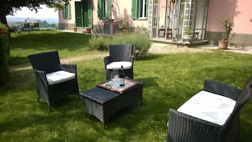Un'area salotto esterna con sedie in vimini e un tavolo, una bottiglia di vino e un bicchiere.