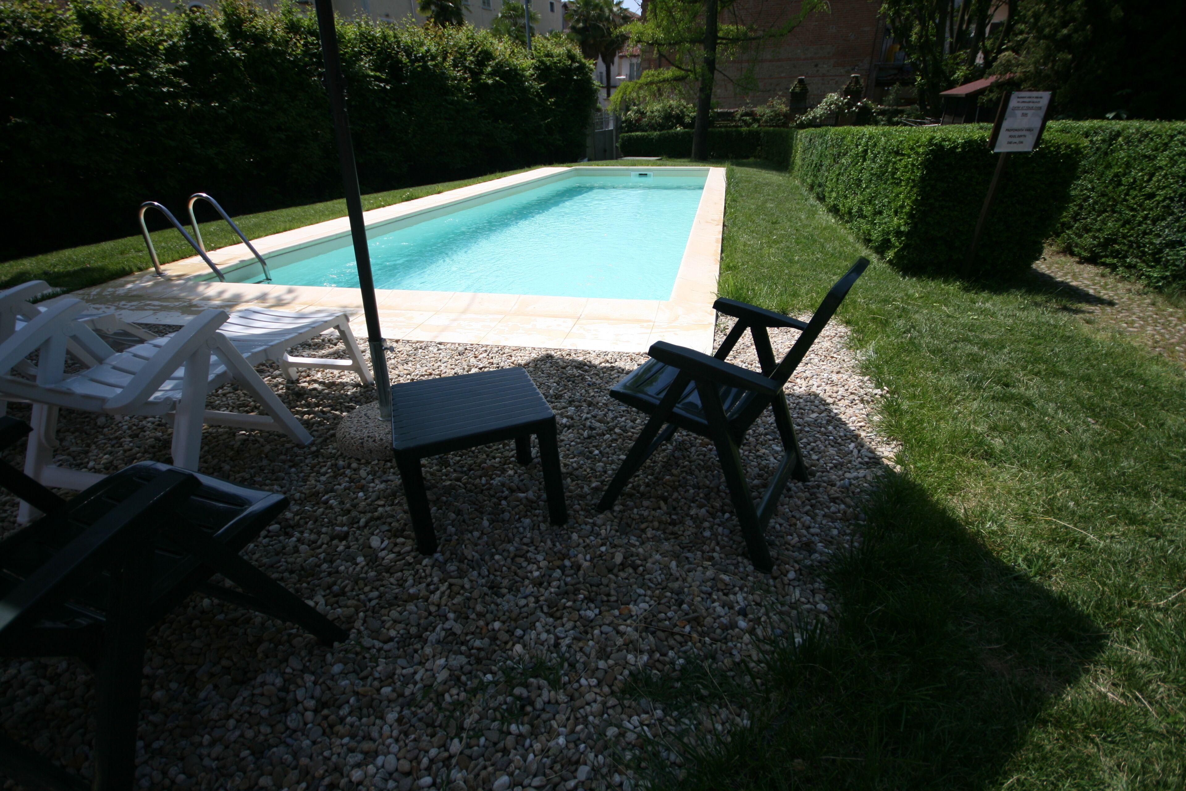 Ein Pool mit Liegestühlen und einem kleinen Tisch, umgeben von Kies und Gras.