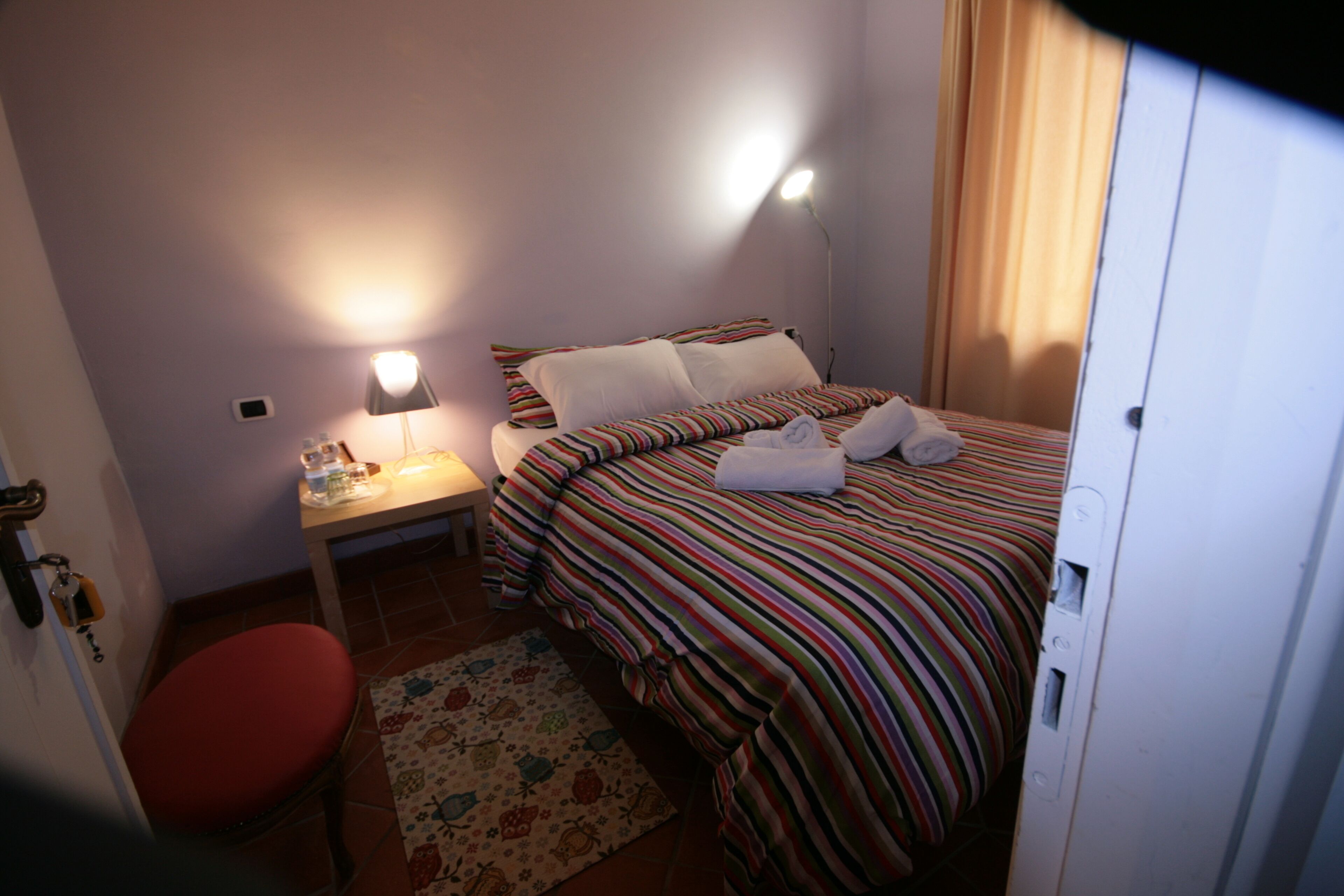 A hotel room with a bed, a nightstand, a lamp, a red chair, and a patterned rug.