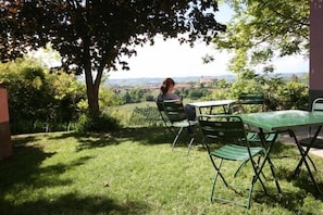 An outdoor seating area with a table and chairs, surrounded by greenery and a view of the countryside.