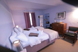 A bedroom with a bed, dresser, chair, and a shelf with books and decorative items.