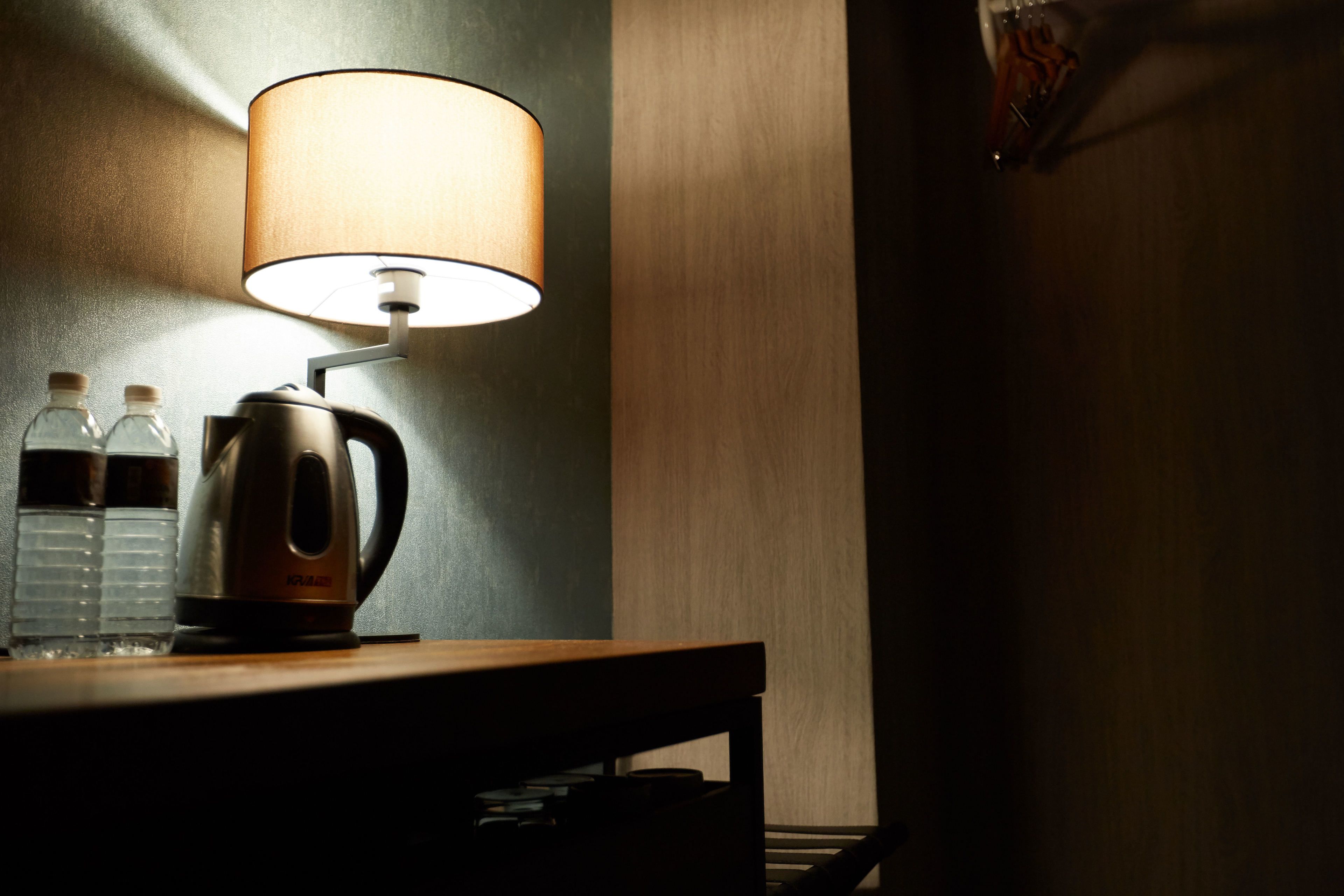 A dimly lit room with a table lamp, a kettle, and two water bottles on a wooden surface.