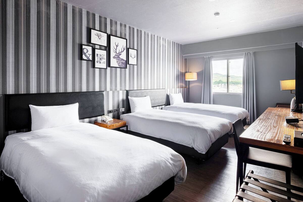 Habitación de hotel con dos camas, un escritorio y una ventana con cortinas.