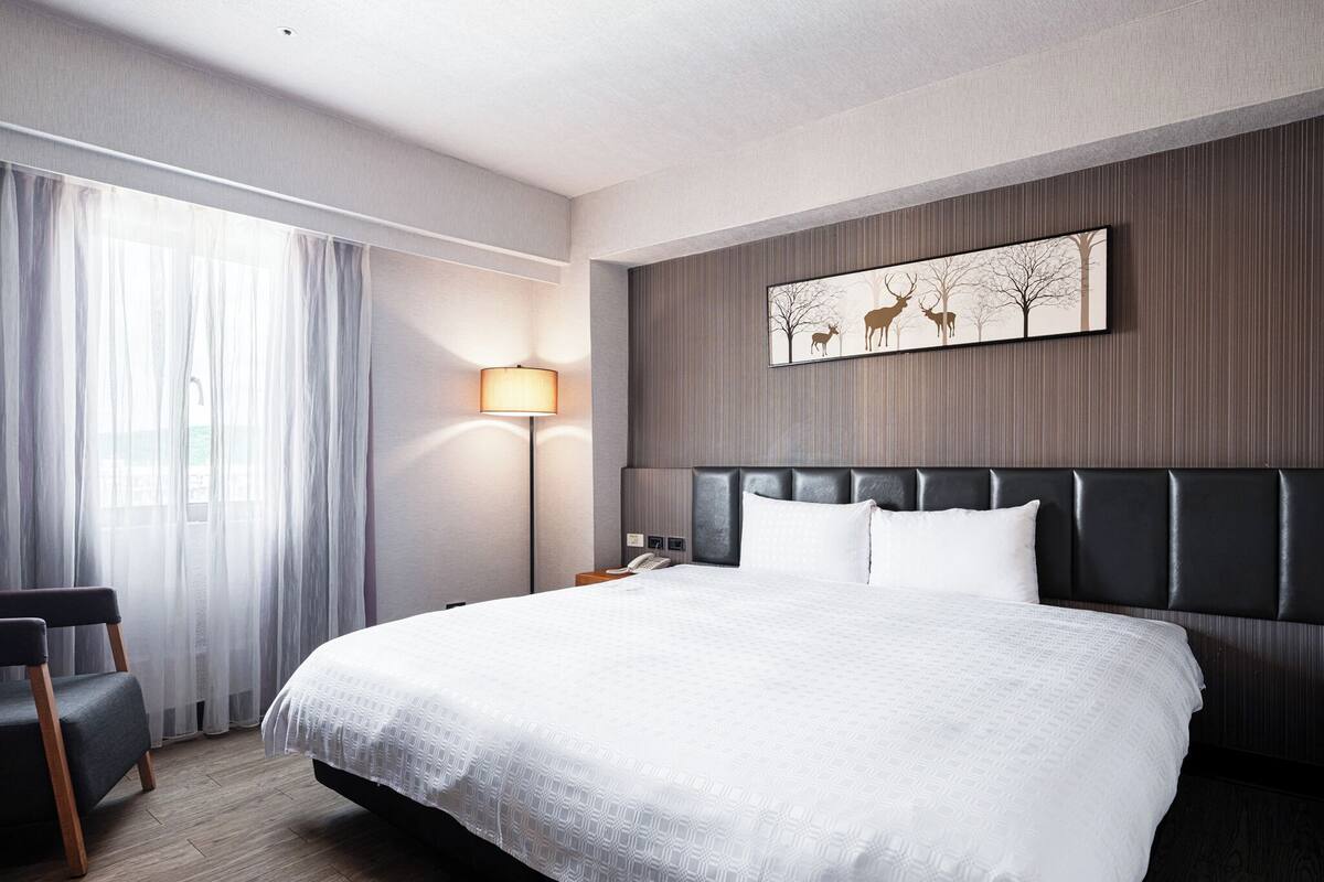 Una habitación de hotel moderna con una cama grande, una mesita de noche, una lámpara y una silla.