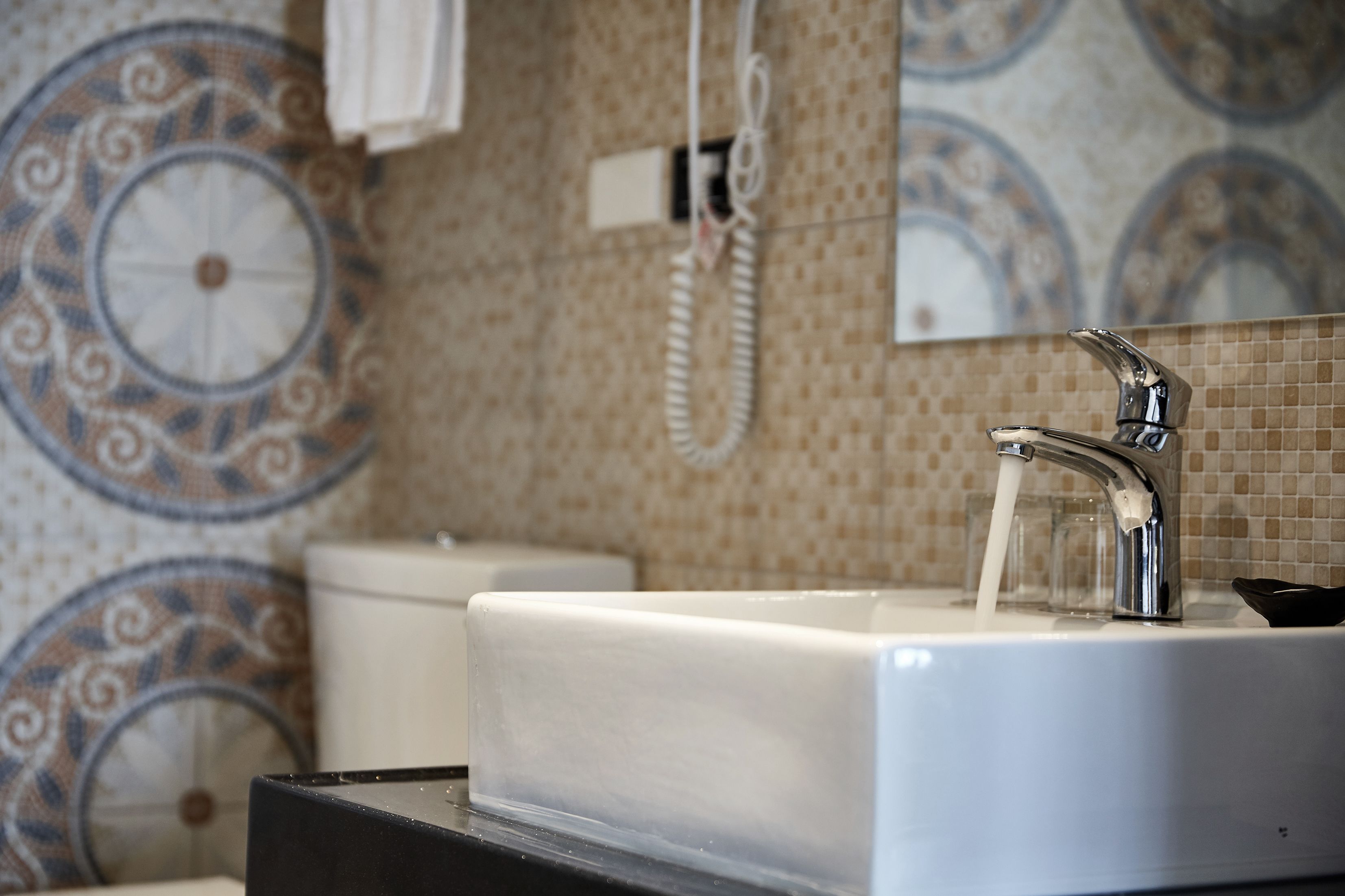 A bathroom with a white sink, chrome faucet, and a patterned tile wall.