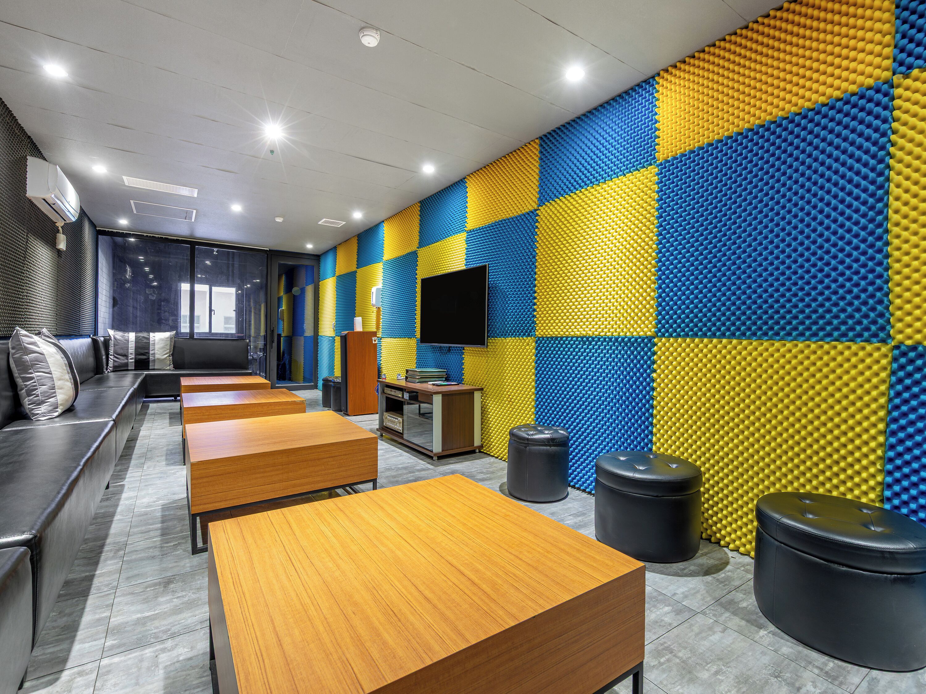 Un intérieur moderne comprenant un espace salon, des tables, un téléviseur et un mur orné d’un motif bleu et jaune.