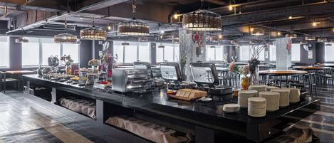 A modern restaurant with a long counter, buffet setup, and industrial-style lighting.