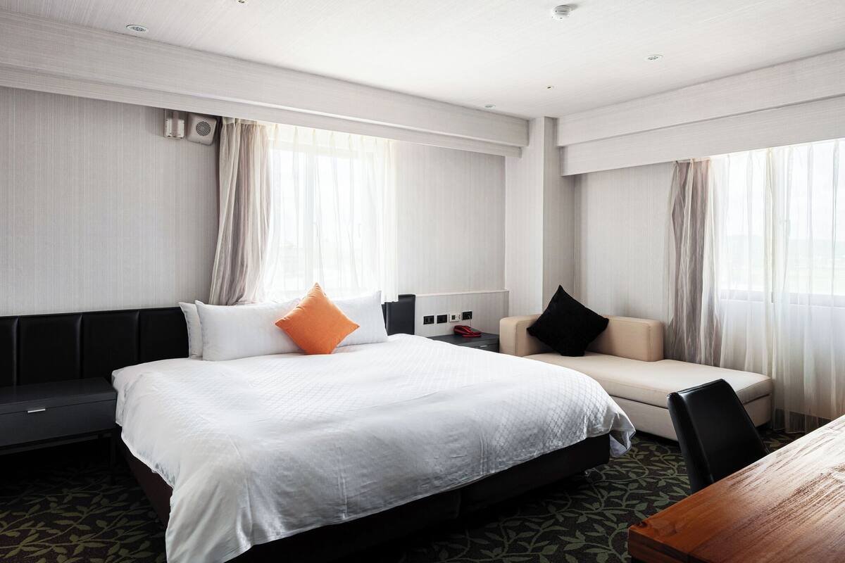 Habitación de hotel con una cama grande, un sofá, una mesa de madera y piso alfombrado.