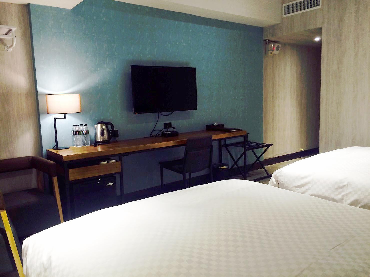 A hotel room with two beds, a desk with a lamp, a television, and a window with curtains.
