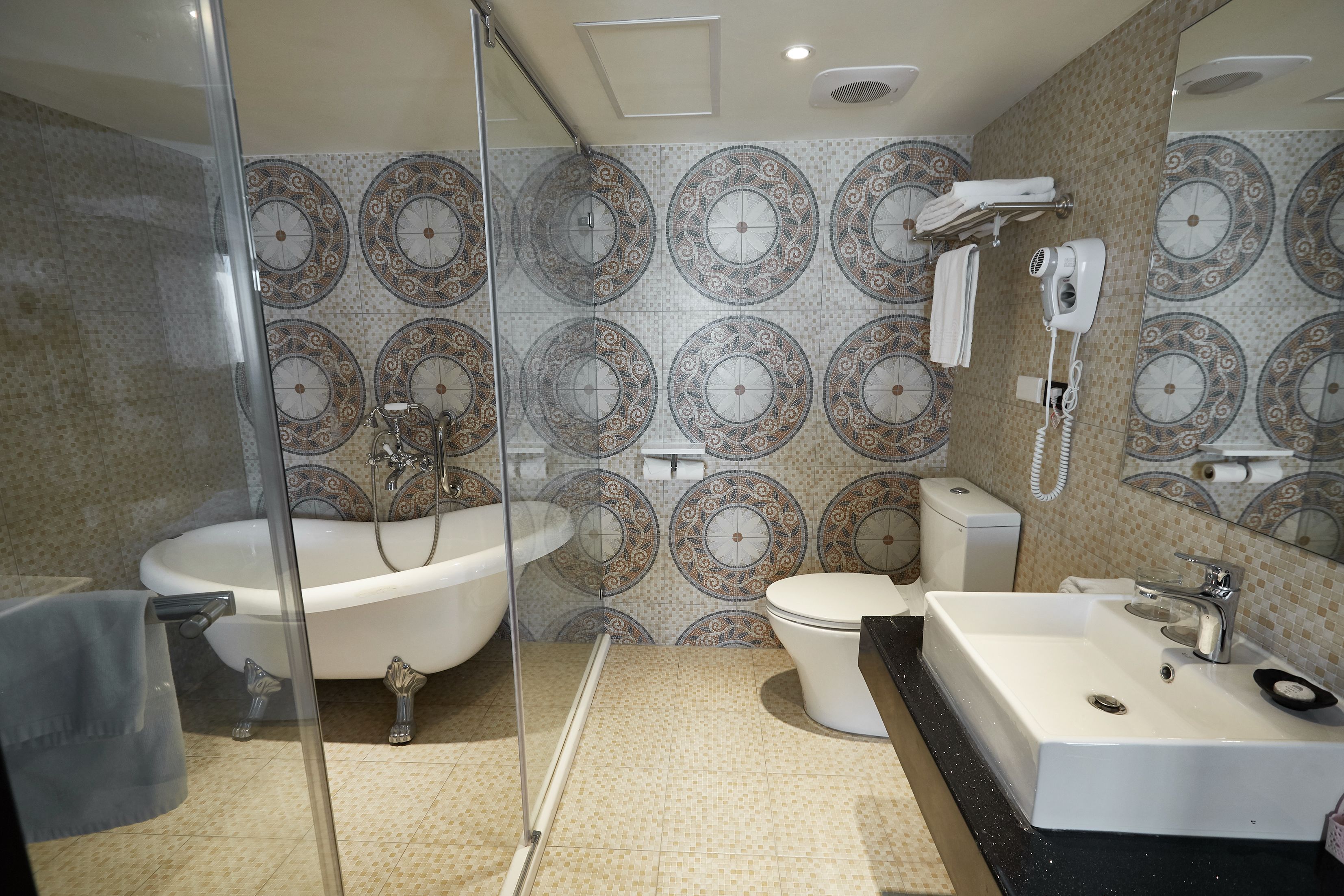 A bathroom with a bathtub, toilet, and sink, featuring patterned tiles and a glass shower enclosure.