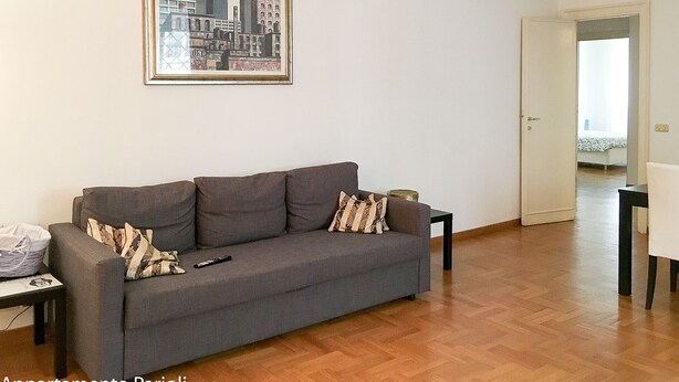 A living room with a grey sofa, a framed cityscape painting, and a wooden floor. - Large apartment suitable for families with children or groups (Roma)