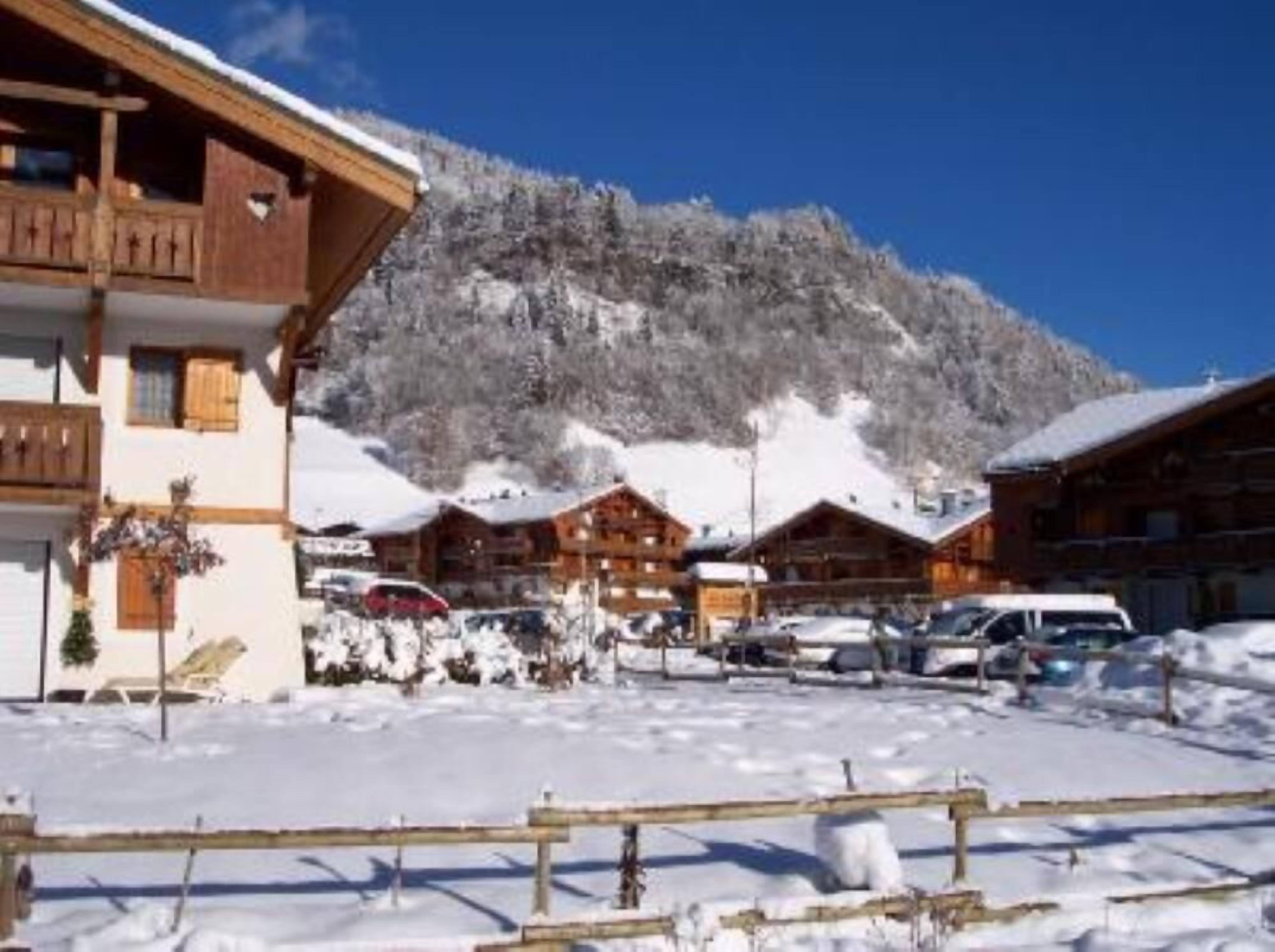 Een houten chalet met een balkon, omringd door een besneeuwde omgeving en een berg op de achtergrond.