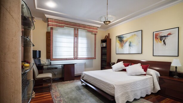 A bedroom with a bed, desk, chair, bookshelf, and artwork on the walls.