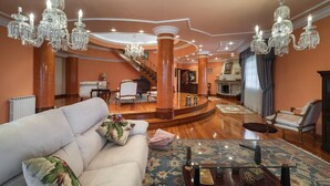 A spacious living room with a large white sofa, a glass coffee table, and a chandelier.