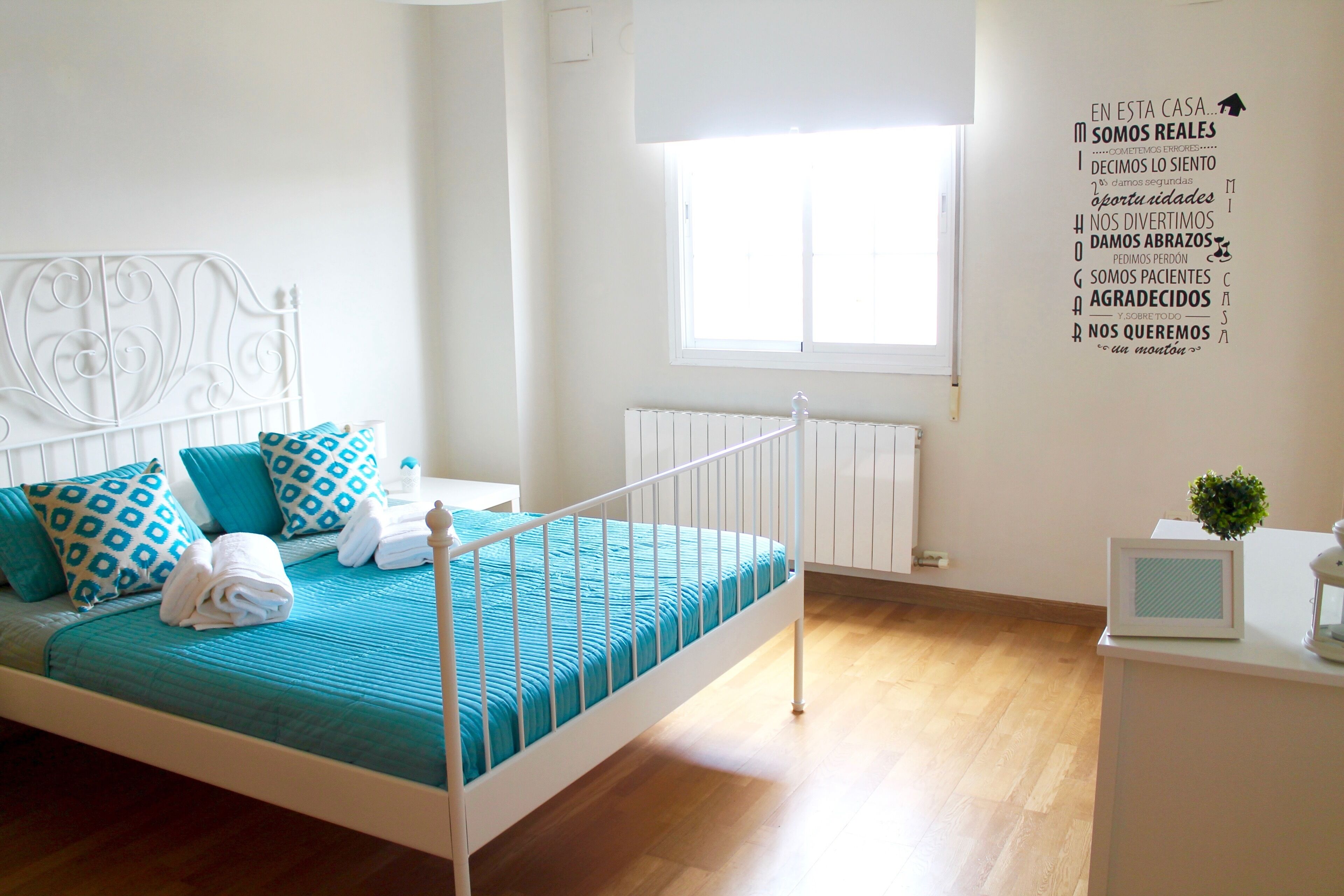 A bedroom with a white metal bed frame, teal bedding, and a window with a view.