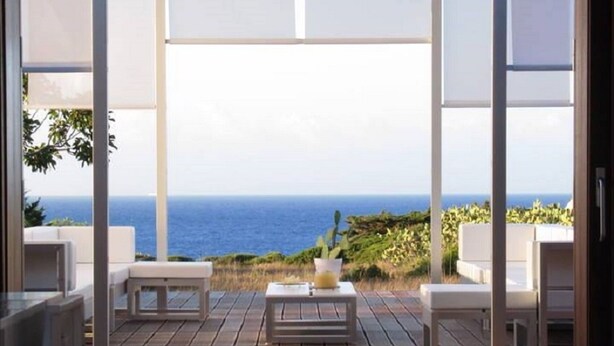 A modern outdoor patio with wooden flooring, white furniture, and a view of the ocean. - Green house (ustica)