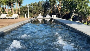 Ein Pool mit Wasserstrahlen, umgeben von Palmen und Liegestühlen.