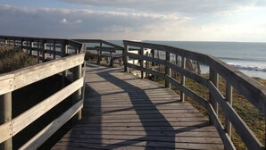 A wooden boardwalk leading to the ocean with a railing on one side.