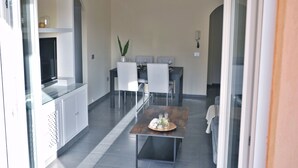 Et moderne spiseområde med et bord med glasplade, hvide stole og en potteplante.