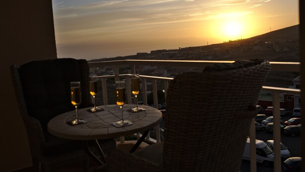 En balkon med et bord dækket til to, med udsigt over en by ved solnedgang.