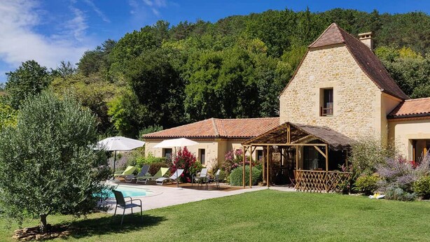 A stone house with a pool, surrounded by greenery and hills.