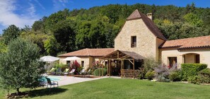 Une maison en pierre avec une piscine, entourée de verdure et de collines.
