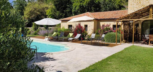 Une piscine avec des chaises longues, une pergola et un bâtiment doté d’un toit en tuiles.