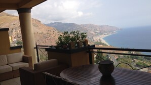 A balcony with a view of the sea and mountains, a table with a bowl, and a sofa. - Fantastic apartment, Taormina with swimming pool, 5 minutes from Greek theater  (Taormina)