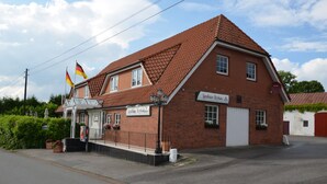 Ein traditionelles Backsteingebäude mit Satteldach, einer Beschilderung mit dem Schriftzug „Landhaus Kroka“ und zwei deutschen Flaggen.