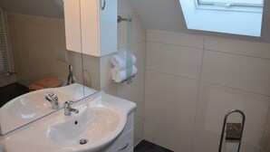 Kylpyhuone, jossa on valkoinen pesuallas, peili ja pyyheteline.