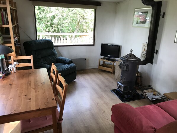 Una sala de estar acogedora con una mesa de madera, un sillón cómodo, un sofá, un televisor y un estufa de leña.