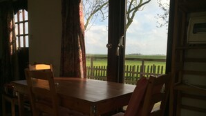 Un comedor con una mesa y sillas de madera, una ventana con cortinas y vistas a un campo verde a través de una valla de madera.