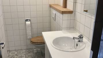 Un baño con un lavabo blanco, inodoro de madera y baldosas de suelo estampadas.