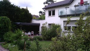 A modern house with a covered patio, a garden with various plants, and a red umbrella.